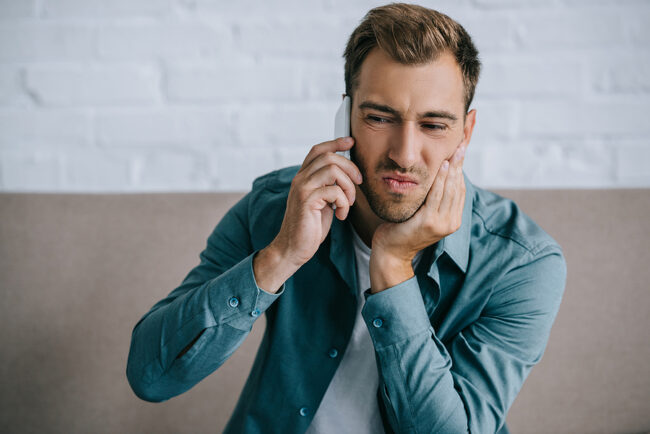 Young Man Talking By Smartphone And Suffering From Jaw Pain At H
